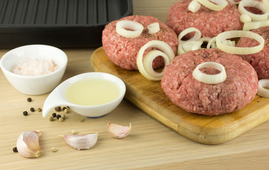 raw burgers, beef on a cooting board, frying pan on woogen backg