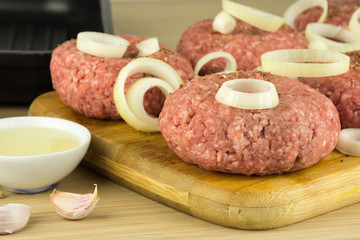 raw burgers, beef on a cooting board, frying pan on woogen backg