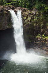 Fototapeta premium Rainbow Falls rushes into a large pool. The waterfall flows over a lava cave