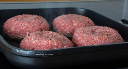 raw burgers, beef in a frying pan on cooking surface in kitchen