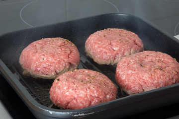raw burgers, beef in a frying pan on cooking surface in kitchen