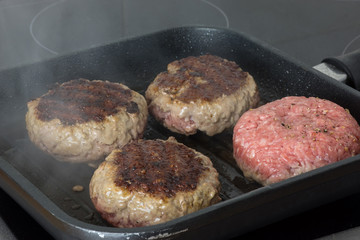 raw burgers, beef in a frying pan on cooking surface in kitchen