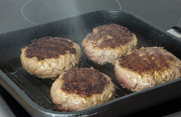 raw burgers, beef in a frying pan on cooking surface in kitchen