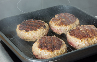 burgers, beef in a frying pan on cooking surface in kitchen