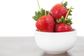 Big strawberry in white bowl right side white background on wood