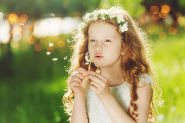Beautiful young child on white dress blowing a dandelion in spri
