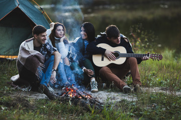 Man playing guitar while sitting with friends at bonfire