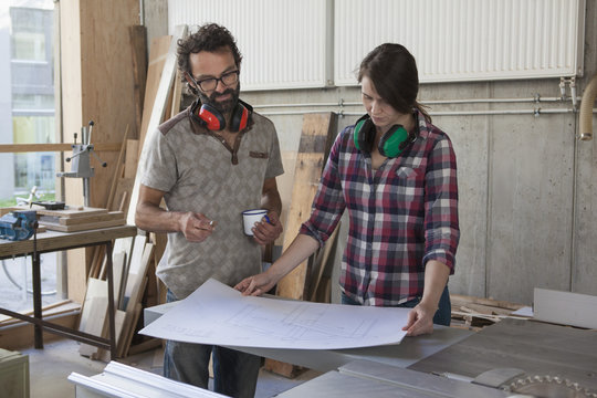 Male and female carpenters with blueprint in workshop