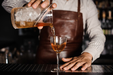 barman pouring alcoholic cocktail in glass