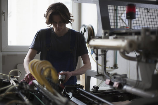 Young manual worker oiling machine in factory