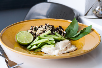 Baked cod with rice and mushrooms of Moher in the Chinese style. Half a lime and basil. Large yellow plate and white table.