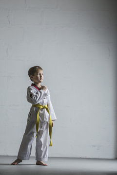 Full length of karate boy standing against white wall