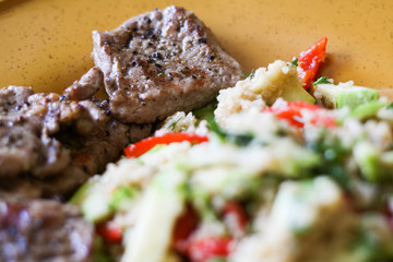 Pork grilled with a side dish of quinoa and grilled vegetables - zucchini and peppers on a large yellow plate.