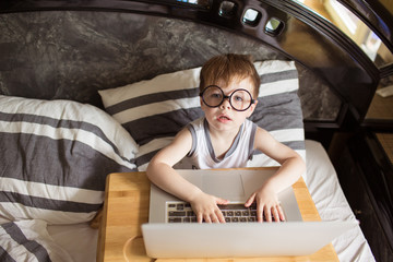 Toddler boy laying on the bed with laptop