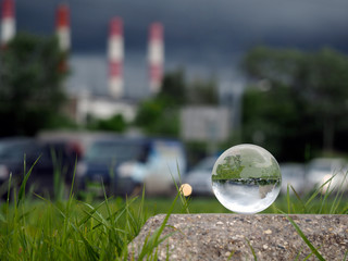 Glass ball on concrete, green grass. Background - pipe heating plant, stormy sky, cars. Concept - gassed cities, smog, harmful emissions into the atmosphere, the environment in big cities 