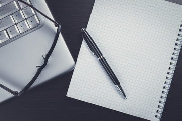 blank notebook, pen, glasses and laptop on the table