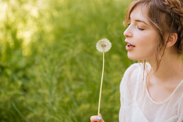 Lovely woman holding and blowing on dandelion outdoors