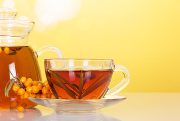 Jug with drink, tea and sprig of sea buckthorn on abstract yellow background.