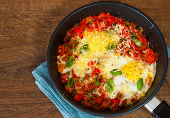 fried eggs with vegetables and cheese in a frying pan on wooden table