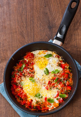 fried eggs with vegetables and cheese in a frying pan on wooden table