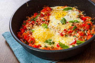 fried eggs with vegetables and cheese in a frying pan on wooden table