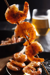 Three grilled shrimp on a stick with light beer glass