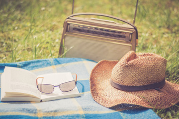 Buch, Strohhut und altes Radio auf Picknickdecke