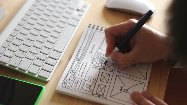 Web designer draws the layout of the site in his book and working on the computer.