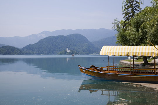 Traditional wooden pletnja (rowing boat) moored on shore to ferry tourists to St. Mary's Church of Assumption on the islet beyond, Lake Bled, Slovenia