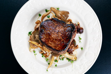 Tasty Beef Mignon steak with mushrooms and herbs on plate.