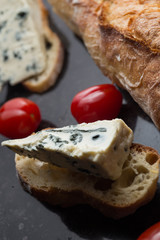 Blue cheese with french baguette, tomato and herbs on black marble table. Traditional snacks in France and Italy.