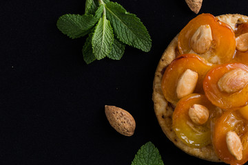 Tart with apricot. Traditional french pie with fruits on dark marble background. Decorated almonds and mint leafs. Delicious dessert with copy space closeup.