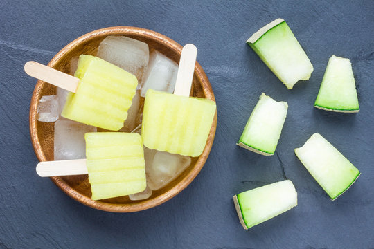 Homemade melon popsicles on grey slate, top view