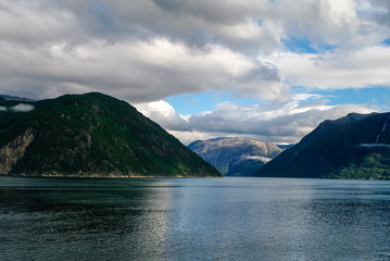 Cloudy sky over banks of fjord. Mountains with green forest, Eidfjord, Norway