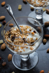 Granola with yoghurt, nuts and fruits in glass bowl on dark background. Delicious, healthy sweet dessert for breakfast. Cereal, muesli.  Copy space, closeup.