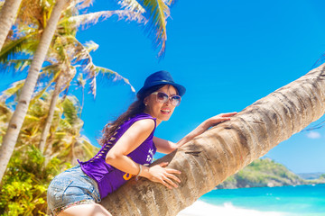 Young beautiful Asian girl on the palm tree on a tropical beach.