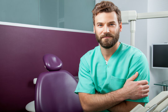 Male doctor with beard in green costume in dental clinic