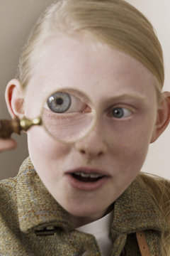 A girl looking surprised as she looks through a magnifying glass