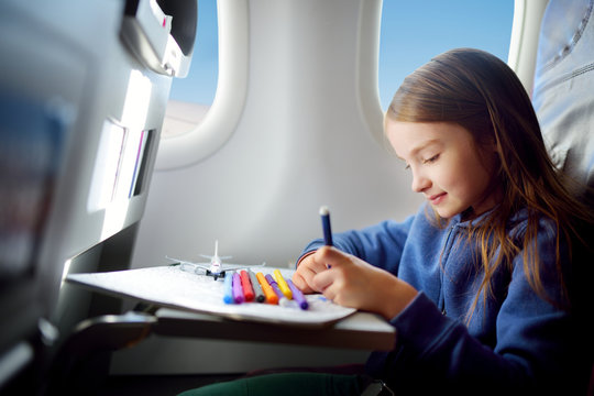 Adorable little girl traveling by an airplane. Child sitting by the window and drawing.