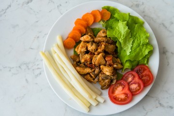 Fried chicken meat served on plate with white asparagus, carrot, tomato and lettuce. Top view