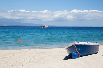 A yaucht in the turquoise sea waters and a blue boat on the white sand