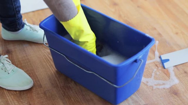 woman washing and squeezing rag in bucket at home