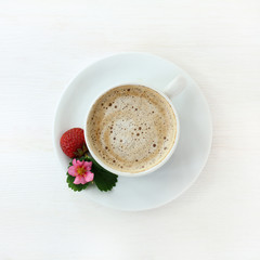 cappuccino garnished with strawberries/ frothy coffee with decoration of fruit, flower and leaf strawberries on a light wooden background top view 