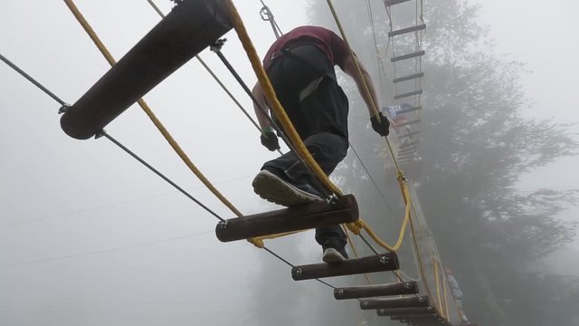 People climbing up the rope ladders in the entertainment park in the forest on a misty or foggy day.  Extreme sports concept.