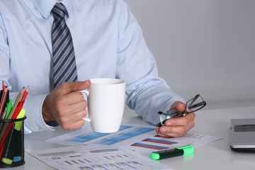 Businessman sitting at office desk having a coffee break and holding a mug