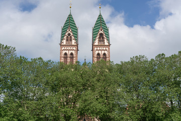 Türme der Herz-Jesu-Kirche in Freiburg mit Bäumen im Vordergrund