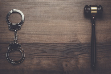 handcuffs and judge gavel on brown wooden background