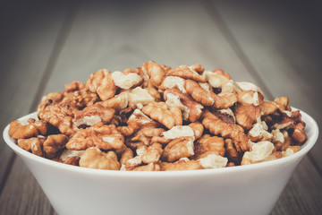 walnuts in the white bowl on brown wooden table