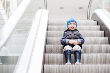 Cute little child sitting on moving staircase