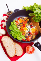 Homemade fried eggs in pan with tomato, bread, pepper, salad and mushrooms on the table